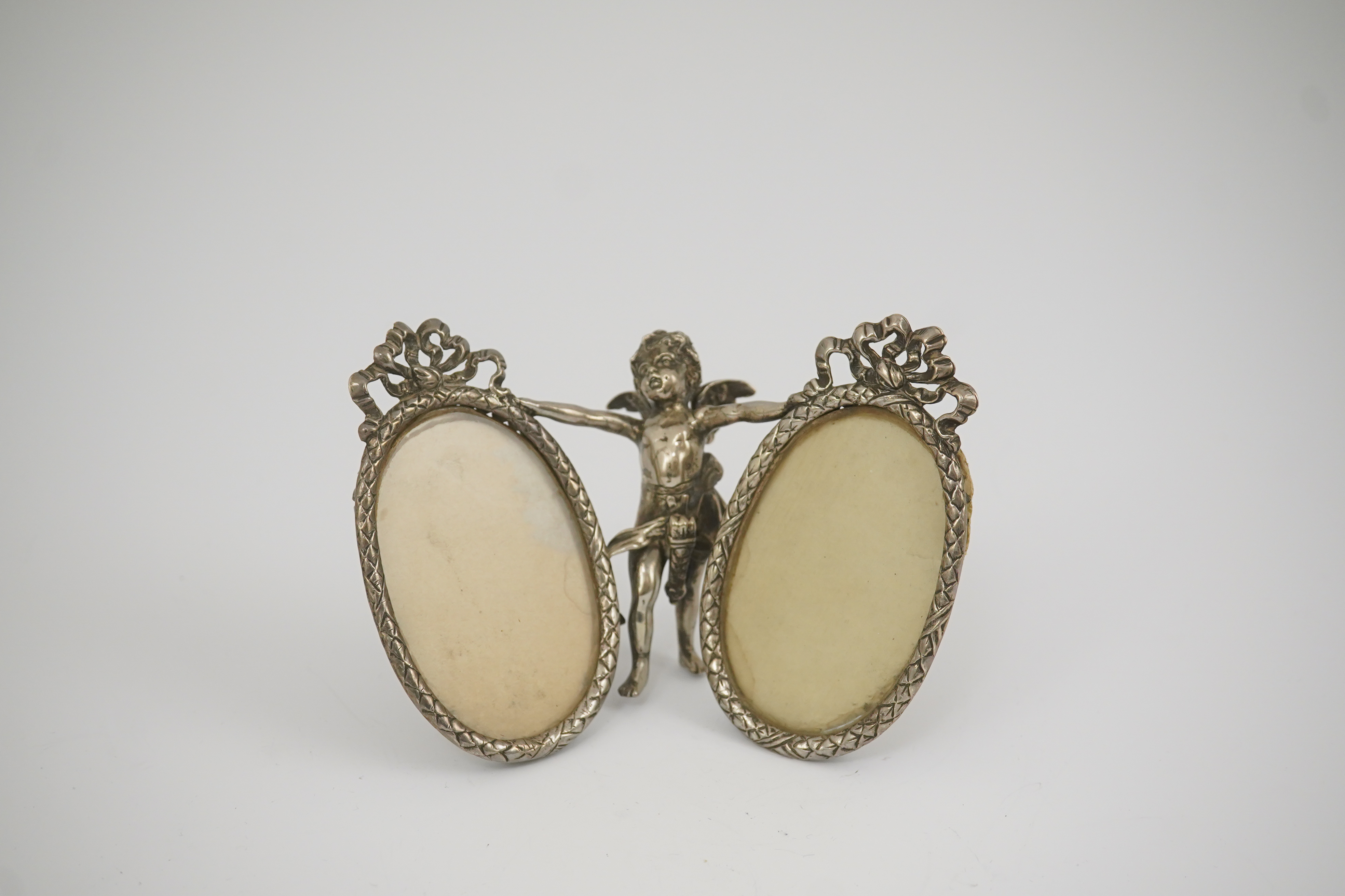 A late 19th century Hanau silver double oval photograph frame, supported by central figure of Cupid, by Berthold Muller